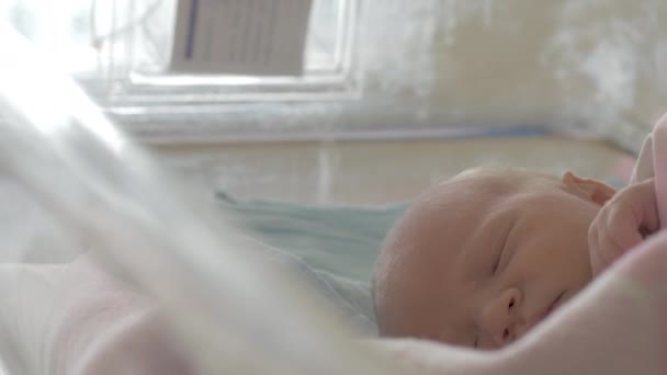 一个刚出生的女孩睡在医院婴儿车在一个明亮的房间里的软粉色毯子下的特写镜头 她的手在睡梦中随意移动 — 图库视频影像