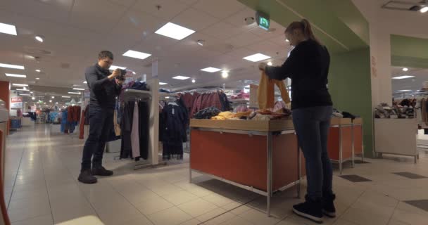 Homme avec une femme de tir mobile choisissant des vêtements pour enfants dans le magasin — Video