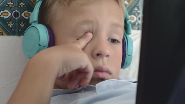 Niño aburrido en auriculares viendo algo en la almohadilla táctil — Vídeo de stock