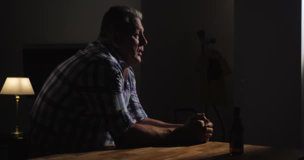 Zdenerwowany starszy człowiek jest sam z butelką piwa w ciemnym pomieszczeniu — Wideo stockowe