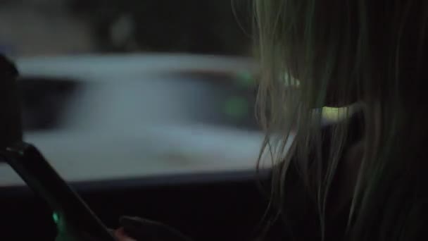 Femme utilisant un téléphone intelligent dans la voiture, vue du soir 