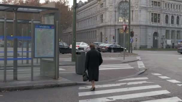 Пожилая женщина идет к автобусной остановке на площади Сибелес в Мадриде, Испания — стоковое видео