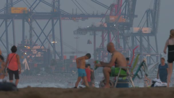 Port z żurawi kontenerowych i zatłoczonej plaży w Walencji, Hiszpania — Wideo stockowe