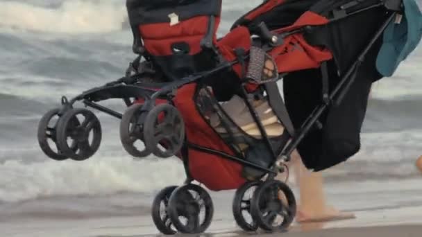 Uma carruagem vermelha do bebê que está sendo movida ao longo da praia — Vídeo de Stock