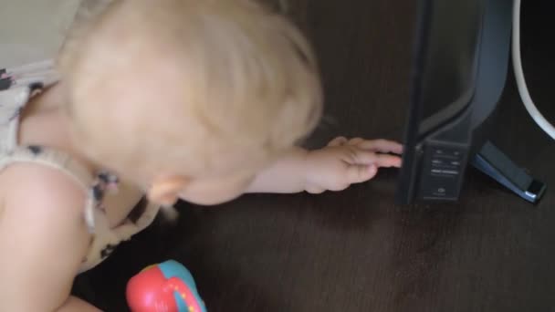 A baby girl in a summer overall examining the TV screen — Stock Video