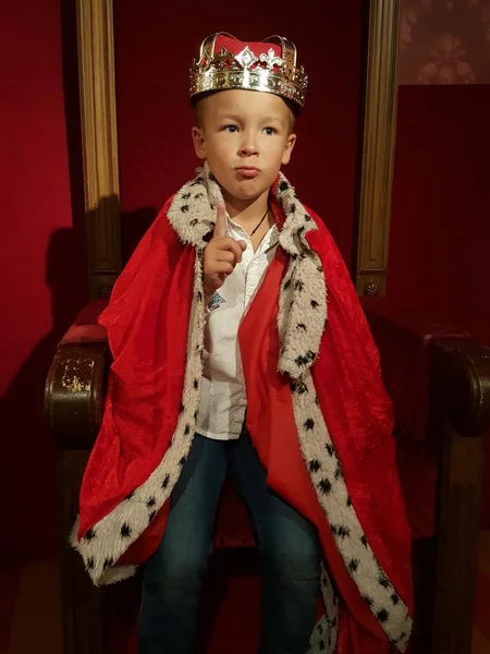 Un petit garçon dans une couronne et un manteau est prêt à régner avec l'index levé — Photo