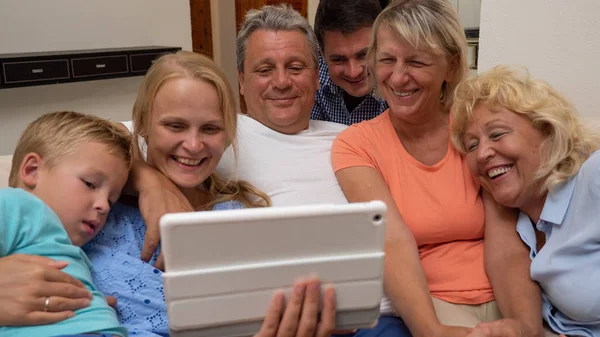 Duża rodzina ogląda coś śmiesznego na podkładce, blisko obok siebie — Zdjęcie stockowe