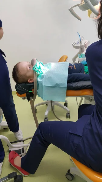 Un fragmento de una sala dental con un niño, acostado en una silla dental, y una parte de sus médicos figura —  Fotos de Stock