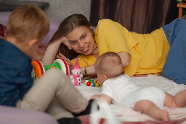 Un nouveau-né couché sur le sol, entouré de ses jouets et de sa famille - une mère et un frère aîné — Photo