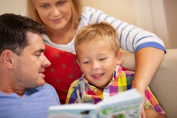 Un niño y sus padres sentados juntos y leyendo un libro —  Fotos de Stock