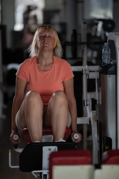 Eine Frau mittleren Alters in einem Fitnessstudio an einem der Trainingsgeräte — Stockfoto