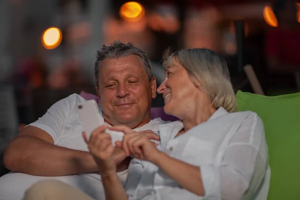 Vrolijke volwassen paar ontspannen buiten en kijken door de mobiele Foto's — Stockfoto