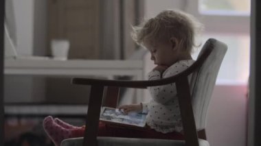 Kucağında tablet olan bir sandalyede oturan bir kız bebek