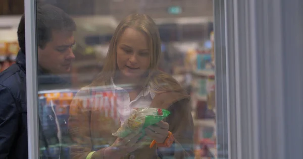 Молодая пара выбирает еду из холодильника в магазине — стоковое фото