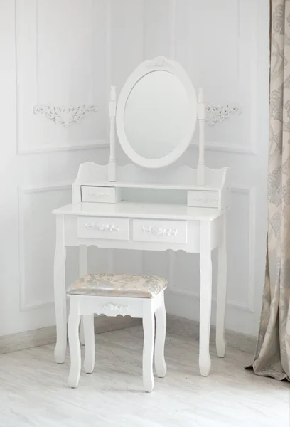 Interior shot of small boudoir dressing table with small mirror and white wooden chair.