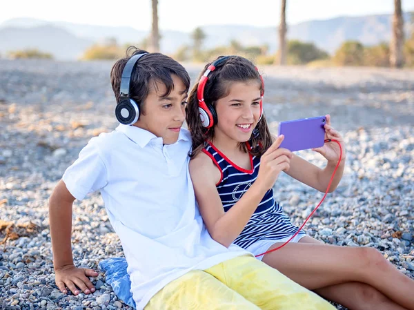 Tieners zitten op het strand met blik van de hoofdtelefoon op de telefoon — Stockfoto