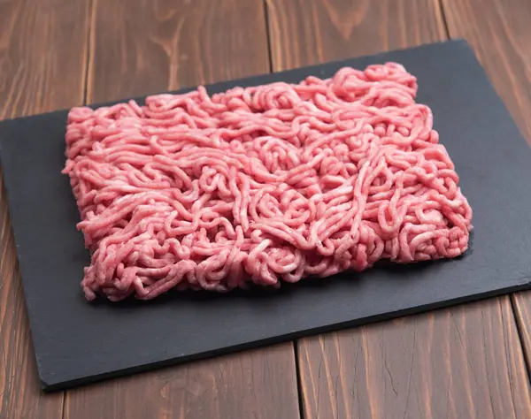 Fresh minced pork on black plate and wooden background. — Stock Photo, Image