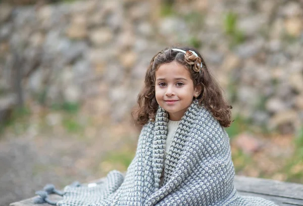 Menina bonita está sentada na natureza e está se aquecendo com um cobertor de malha quente — Fotografia de Stock