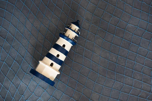 Little toy lighthouse on a dark background with a sea grid. — Stock Photo, Image