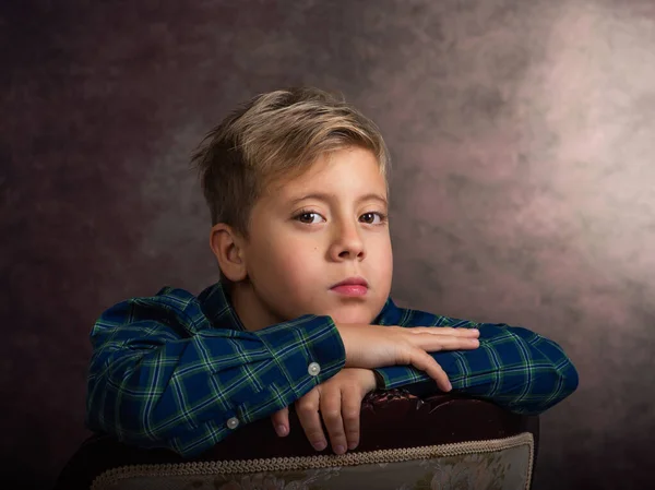 Schöner kleiner Junge, blond, traurig, auf einem Stuhl lehnend. — Stockfoto