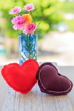 Kahverengi ve kırmızı kalp şekli yastık ile doğa arka plan ile ahşap tahta üzerinde mavi vazo içinde güzel bir pembe ve sarı moss gül.