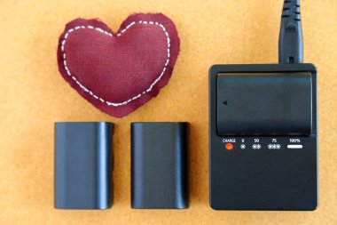 Fotoğraf makinesi lithium-Ion pili şarj cihazı üzerinde ahşap masa üzerinde kahverengi kalp yastık ile şarj.