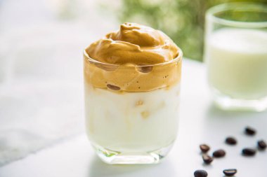 Bulanık kahve çekirdekli bir fincan Dalgona kahvesi ve öğleden sonra bulanık arkaplanlı beyaz bir masada bir fincan süt..