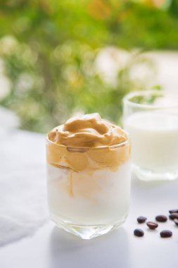 Bir fincan Dalgona kahvesini kapayın. Yanında kahve çekirdekleri olsun. Beyaz bir masanın üzerinde..