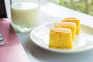 Tereyağlı kek paketini beyaz bir tabakta pembe bir dizüstü bilgisayarın yanına koy..