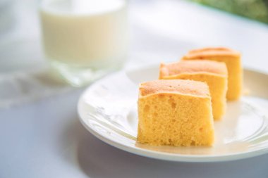 Tereyağlı kek yığınını beyaz bir tabakta, arka planda bulanık bir bardak sütle kapat..