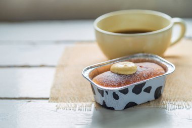 Yan manzaraları kapatın. Bir fincan kremalı Hokkaido sütlü ekmeği ve beyaz ahşap masa üzerinde bir fincan kahveyi kapayın. Pencereden gelen ışıkla..