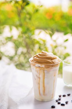 Bir fincan Dalgona kahvesini kapayın. Yanında kahve çekirdekleri olsun. Beyaz bir masanın üzerinde..