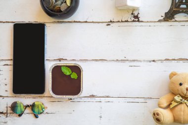 Üzerinde nane şekerlemesi olan çikolatalı pasta, beyaz ahşap bir masa, cep telefonu, dekorasyon ve oyuncak ayı. Metin için boşluk 