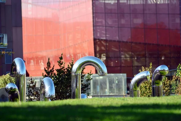 Public art installation in front modern building.Decorative stainless steel pipes