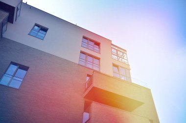 Mavi gökyüzü olan güneşli bir günde modern apartman binaları. Modern bir apartmanın ön cephesi. Güneş ışığıyla kaplı cam yüzey..