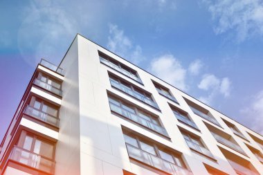 Mavi gökyüzü olan güneşli bir günde modern apartman binaları. Modern bir apartmanın ön cephesi. Güneş ışığıyla kaplı cam yüzey..