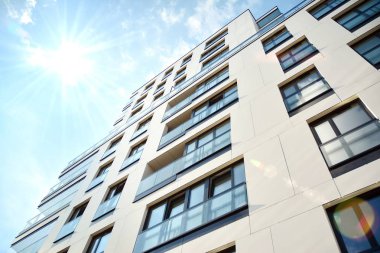 Mavi gökyüzü olan güneşli bir günde modern apartman binaları. Modern bir apartmanın ön cephesi. Güneş ışığıyla kaplı cam yüzey..
