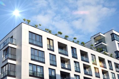 Mavi gökyüzü olan güneşli bir günde modern apartman binaları. Modern bir apartmanın ön cephesi. Güneş ışığıyla kaplı cam yüzey..