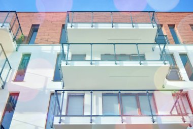 Mavi gökyüzü olan güneşli bir günde modern apartman binaları. Modern bir apartmanın ön cephesi. Güneş ışığıyla kaplı cam yüzey..