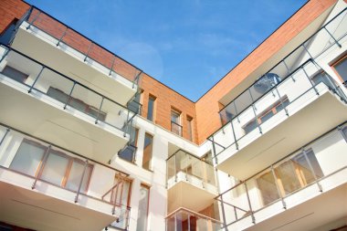 Mavi gökyüzü olan güneşli bir günde modern apartman binaları. Modern bir apartmanın ön cephesi. Güneş ışığıyla kaplı cam yüzey..