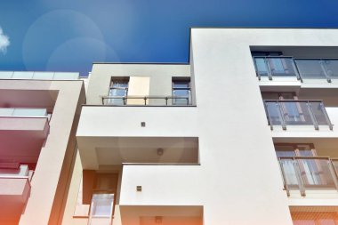 Mavi gökyüzü olan güneşli bir günde modern apartman binaları. Modern bir apartmanın ön cephesi. Güneş ışığıyla kaplı cam yüzey..