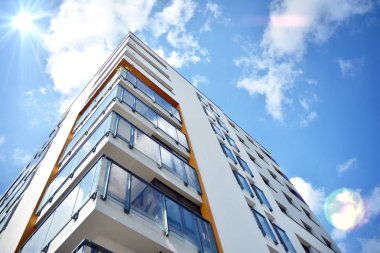 Mavi gökyüzü olan güneşli bir günde modern apartman binaları. Modern bir apartmanın ön cephesi. Güneş ışığıyla kaplı cam yüzey..