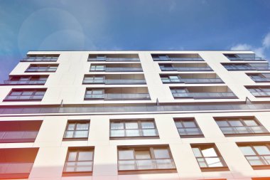 Mavi gökyüzü olan güneşli bir günde modern apartman binaları. Modern bir apartmanın ön cephesi. Güneş ışığıyla kaplı cam yüzey..