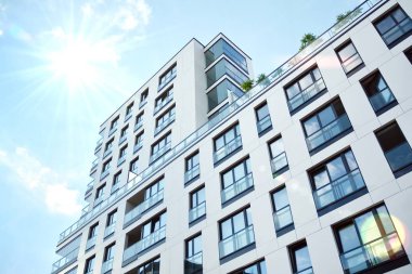 Mavi gökyüzü olan güneşli bir günde modern apartman binaları. Modern bir apartmanın ön cephesi. Güneş ışığıyla kaplı cam yüzey..