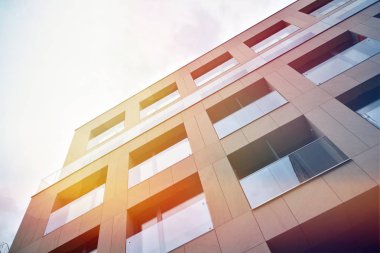 Mavi gökyüzü olan güneşli bir günde modern apartman binaları. Modern bir apartmanın ön cephesi. Güneş ışığıyla kaplı cam yüzey..