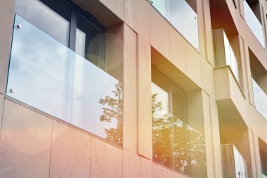 Mavi gökyüzü olan güneşli bir günde modern apartman binaları. Modern bir apartmanın ön cephesi. Güneş ışığıyla kaplı cam yüzey..