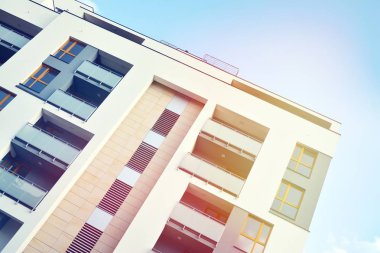 Mavi gökyüzü olan güneşli bir günde modern apartman binaları. Modern bir apartmanın ön cephesi. Güneş ışığıyla kaplı cam yüzey..