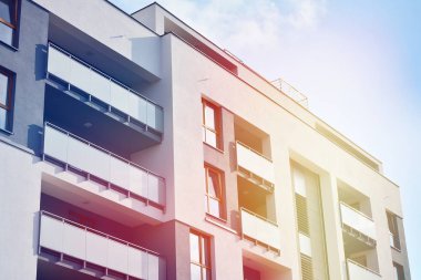 Mavi gökyüzü olan güneşli bir günde modern apartman binaları. Modern bir apartmanın ön cephesi. Güneş ışığıyla kaplı cam yüzey..