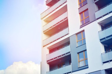Mavi gökyüzü olan güneşli bir günde modern apartman binaları. Modern bir apartmanın ön cephesi. Güneş ışığıyla kaplı cam yüzey..