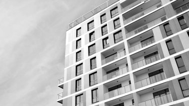 Pencereleri ve balkonları olan bir binanın ön cephesi. Birçok dairesi olan modern bir ev. Siyah ve beyaz.